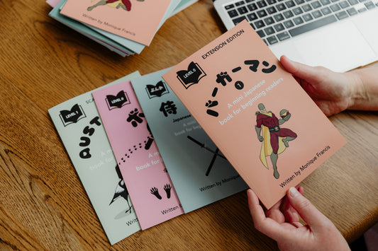 Several JapanEasyReads books stacked on a desk, with a person holding some of the books, showing colorful covers and beginner-friendly graded Japanese reading materials.